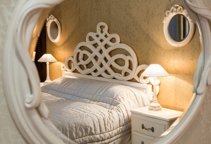 White vintage style carved bed and nightstand with lamps sen through the carved mirror